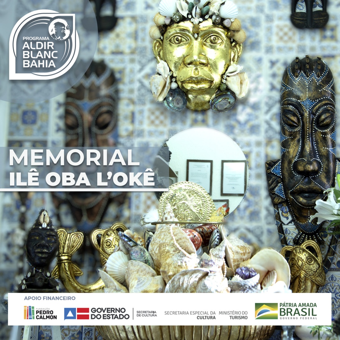 Eine Ausstellung traditioneller kultureller Artefakte, darunter kunstvolle goldene und schwarze Masken und zeremonielle Objekte, die an einer physischen Gedenkstätte namens 'Memorial Ilê Oba L'Okê' arrangiert sind.